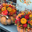 Load image into Gallery viewer, Two orange pumpkins arranged on a gray porch railing, filled with colorful autumn floral arrangements including small pumpkins, roses, chrysanthemums, berries, and fall leaves. A white pillow with an autumn leaf design and the words 'Welcome Autumn' is visible in the background.
