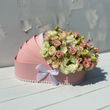Load image into Gallery viewer, A pink round flower box filled with a bouquet of pale pink and cream roses, eustoma, and green buds, tied with a white bow and decorated with a pearl-like border, set on a white wooden surface.
