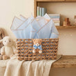 Load image into Gallery viewer, A woven wicker gift basket with a teddy bear plush and blue tissue paper, styled on a wooden shelf in a cozy nursery setting.
